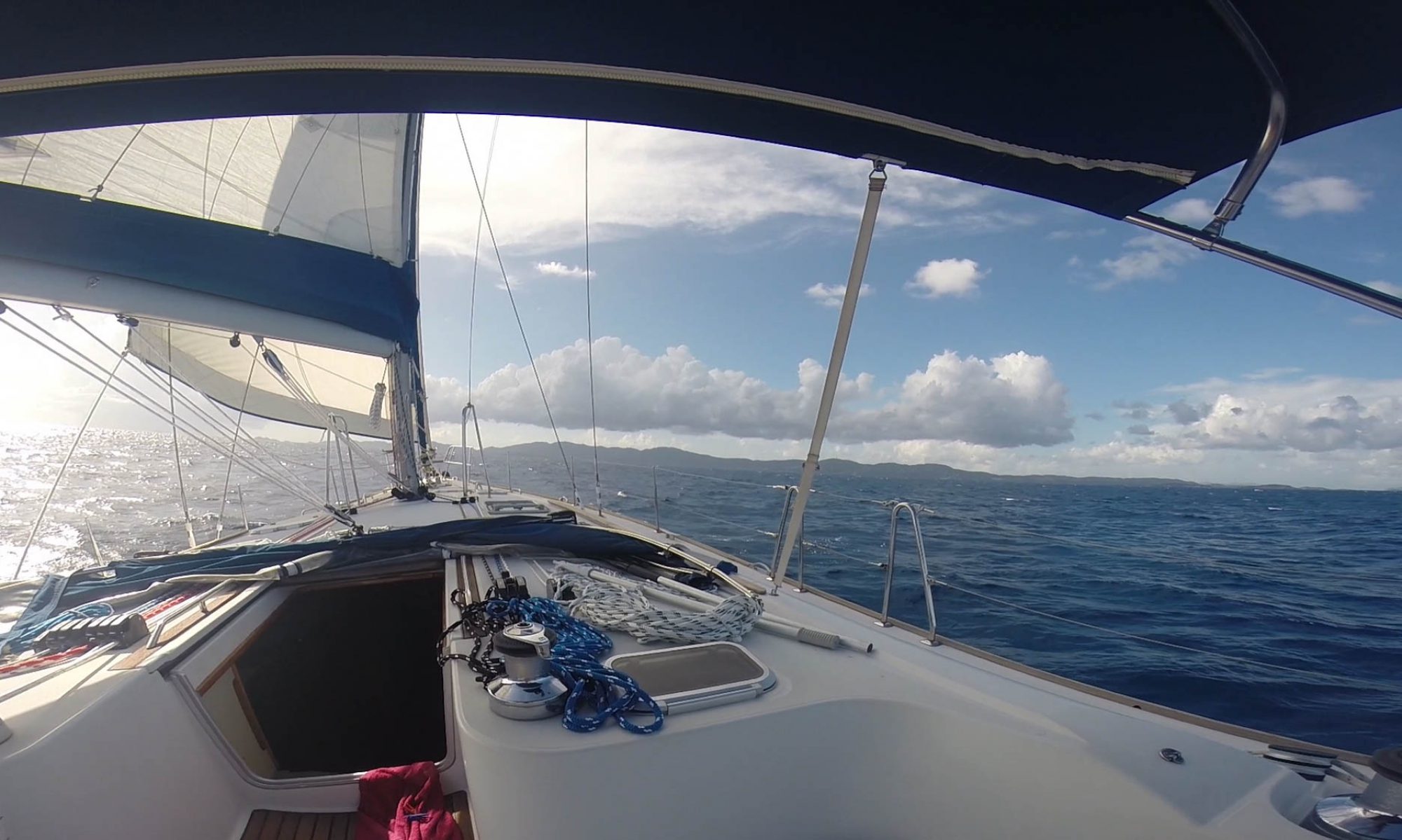 Looking out from a sailboat under full sail at a beautiful blue ocean with the British Virgin Islands in the distance